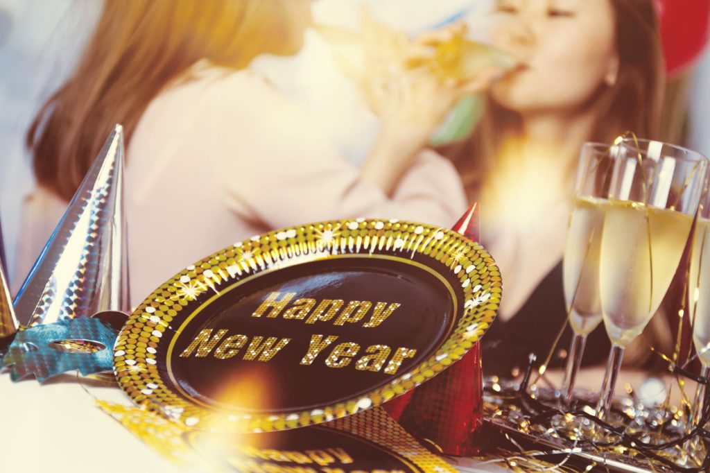 A decorative bowl with HAPPY NEW YEAR printed on it. In the background, two women drink champagne.